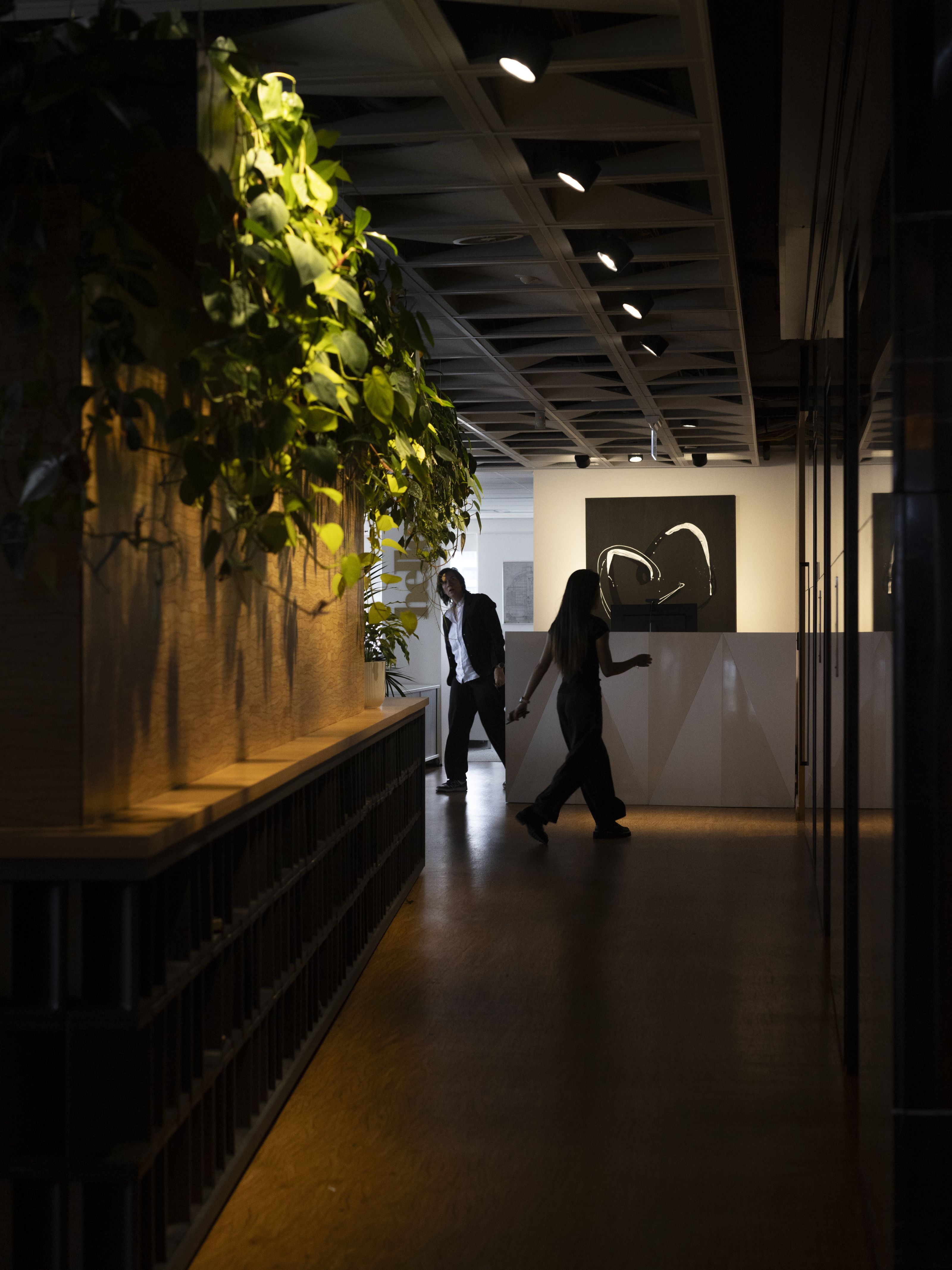 Two people walking through a planted office corridor with feature lighting
