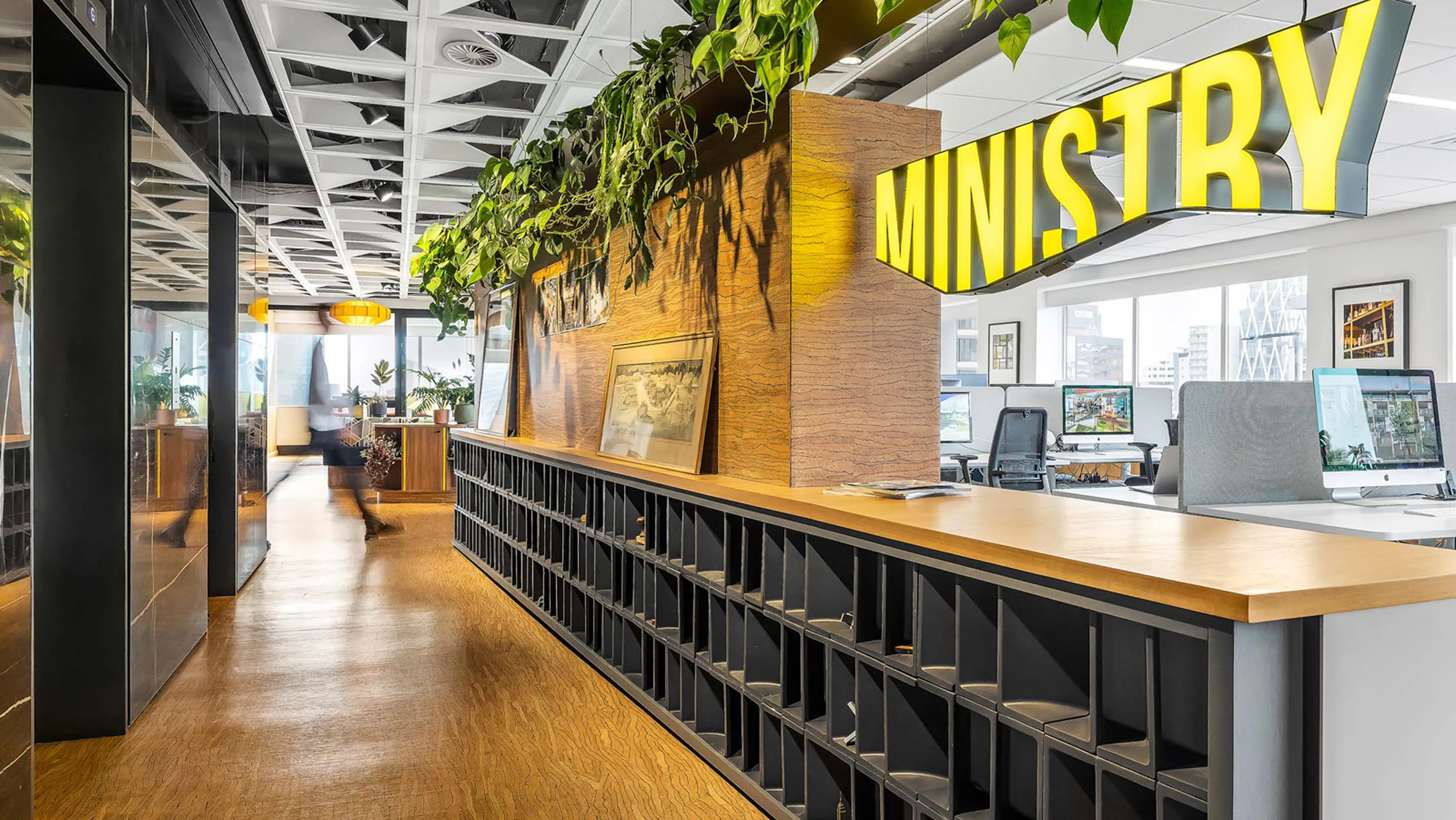 Ministry studio with a yellow MINISTRY sign, trailing planting and a long shared work bench