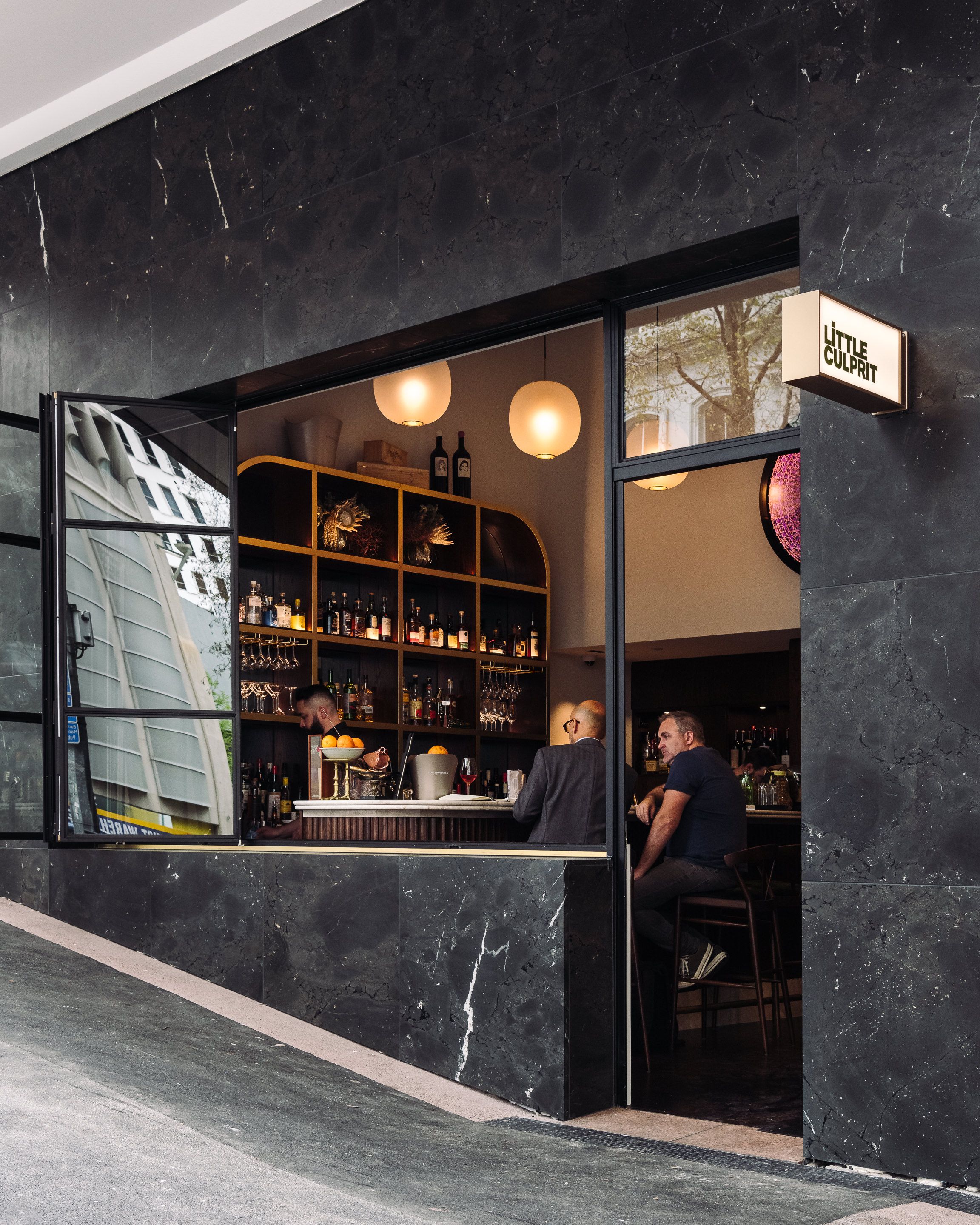 Little Culprit street frontage in dark marble, with a window onto the bar and shelves of bottles