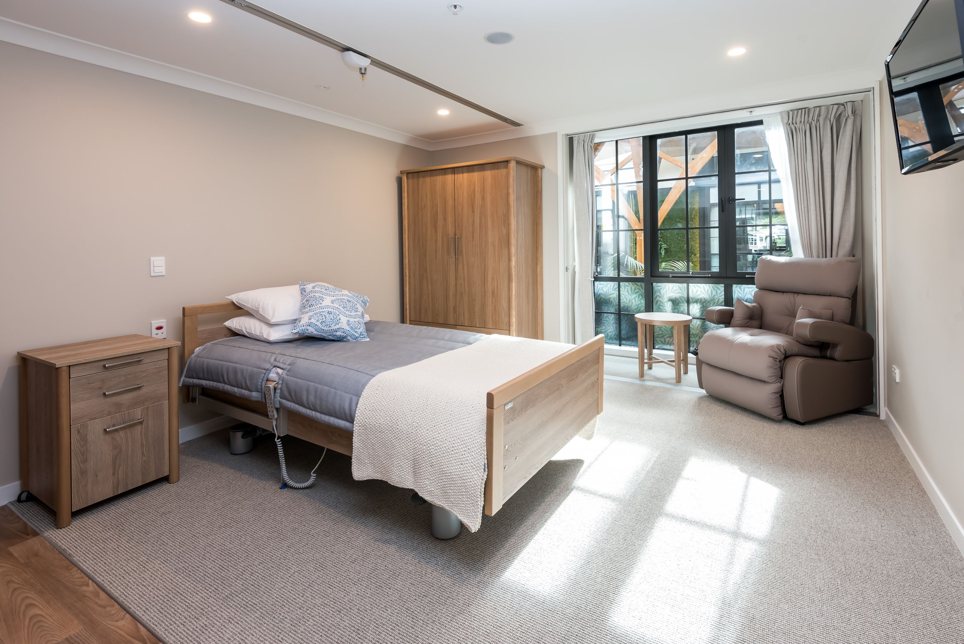 Aged care bedroom at Rawhiti Estate with a care bed, recliner chair and doors to a private balcony