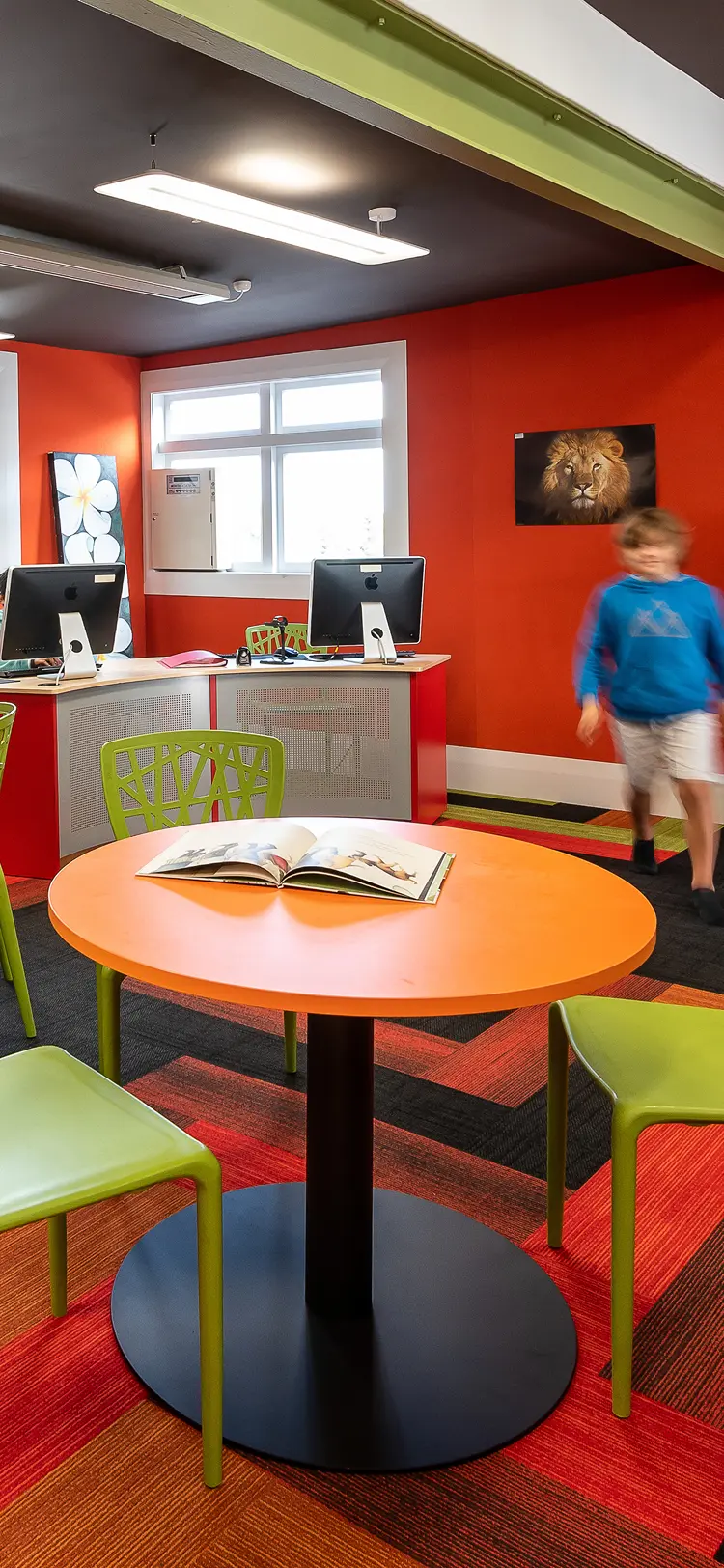 School library interior with bright orange walls, lime-green chairs and children reading at round tables