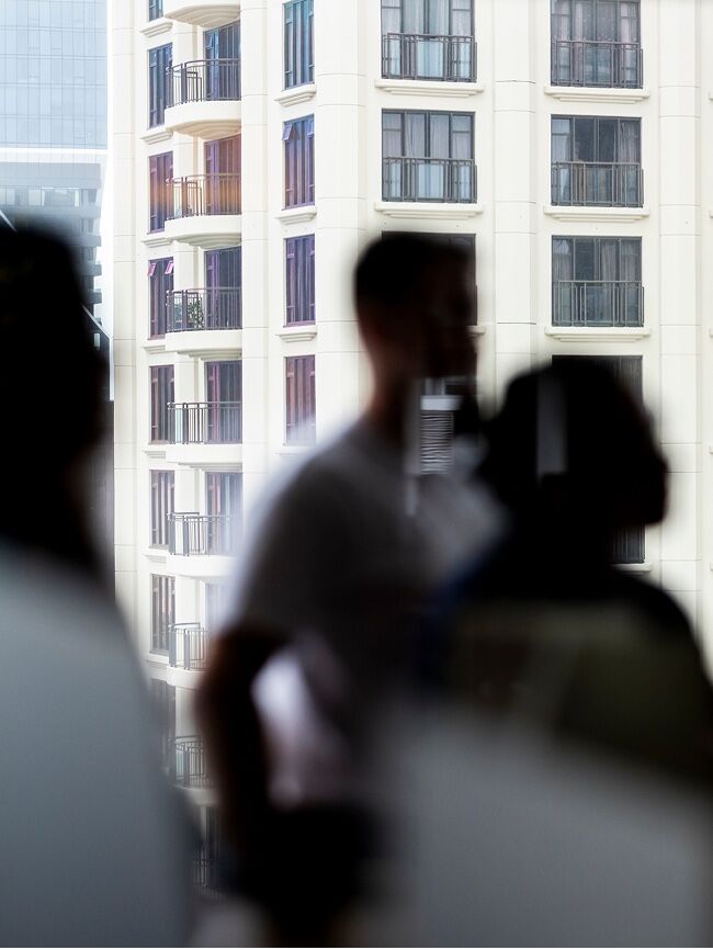 Apartment tower seen through a window, with figures in soft focus in the foreground