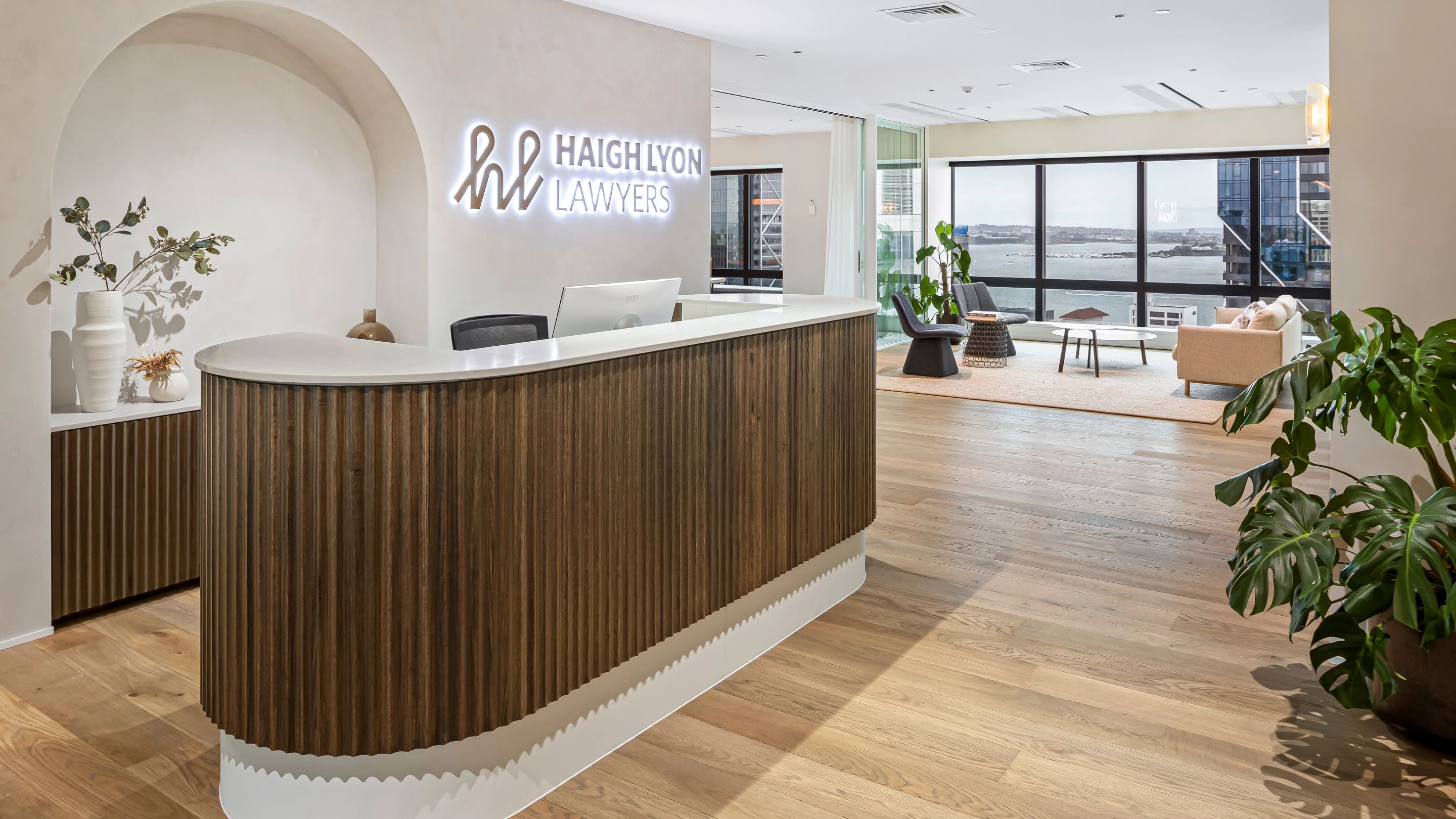 Haigh Lyon reception with a curved fluted timber desk, brand signage and harbour views beyond