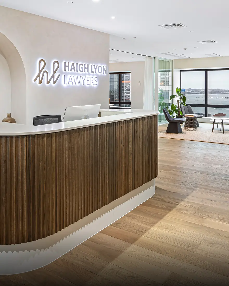 Haigh Lyon reception: fluted timber desk under a backlit logo, with harbour views beyond